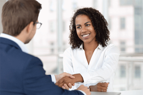 Smiling female human resources manager shakes the hand of a male job candidate whose back is turned to the camera.